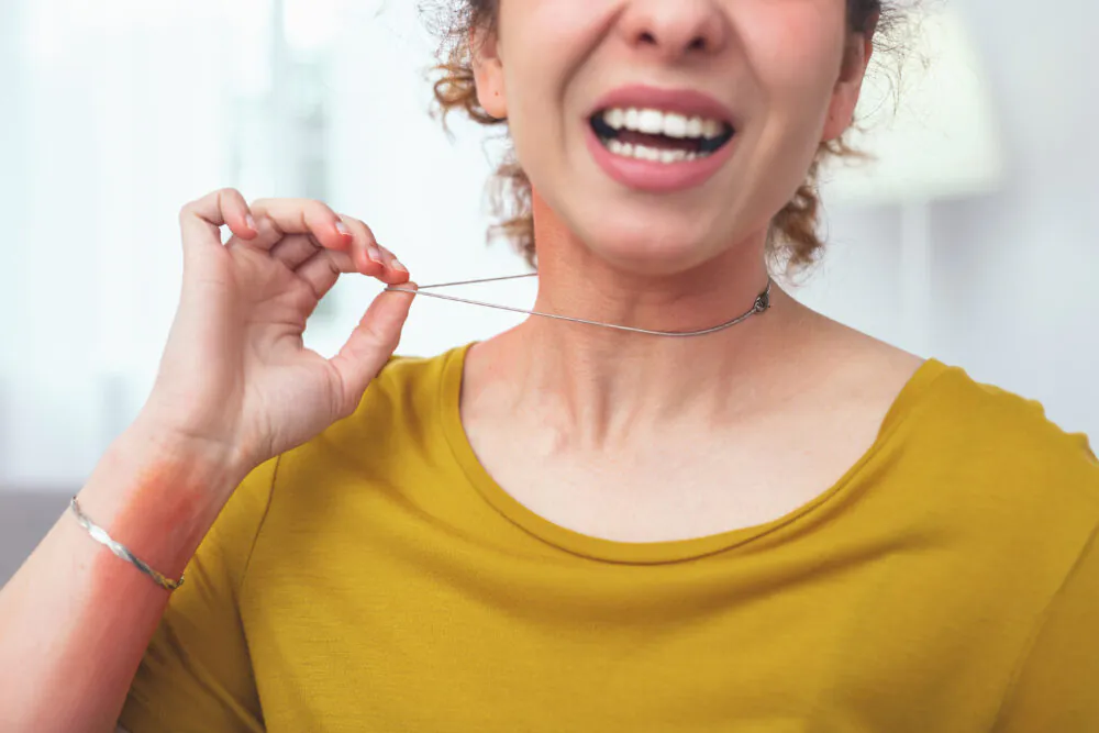 Low-quality metal. Young lady looking sore and unwell while holding on to her low-quality necklace causing her skin have allergic response