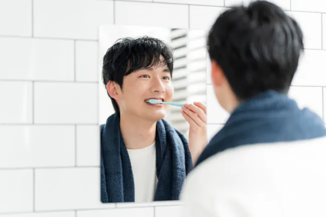 鏡を見ながら丁寧に歯磨きする男性