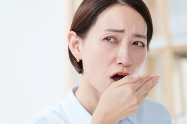 インプラント治療後に口臭を感じて口に手をあてて臭いを確認している女性