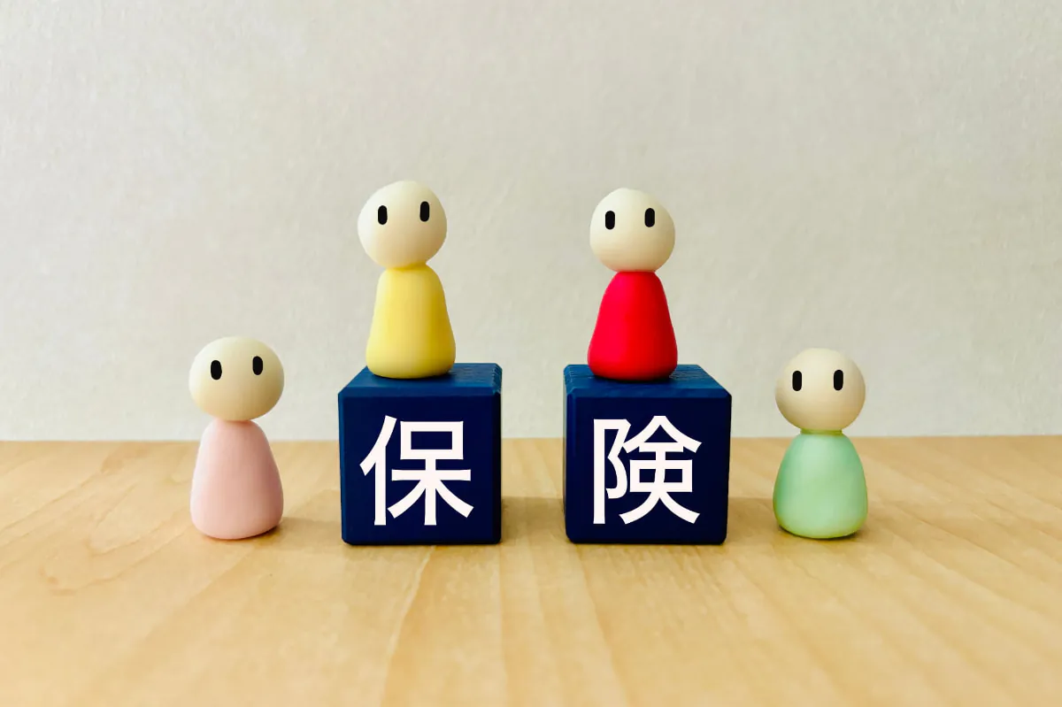 保険の文字の書かれた青いブロックを囲む人形達